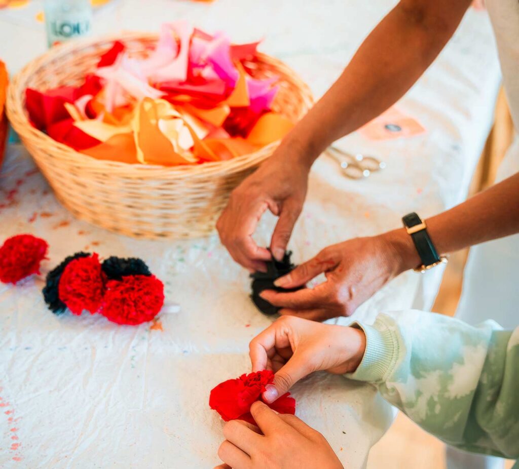 Två par händer pysslar med mexikanska pappersblommor.