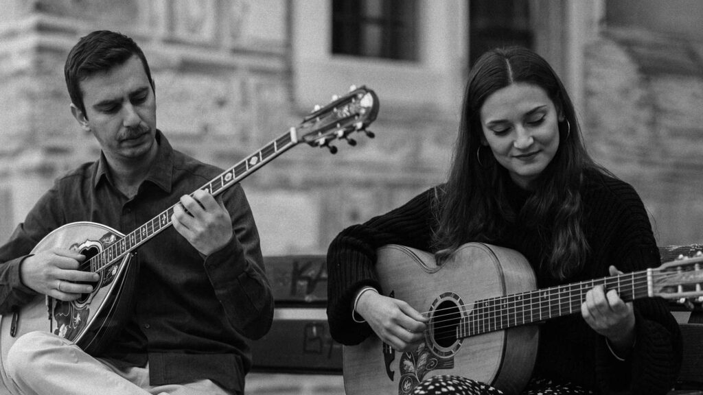 Två musiker på en bänk: en man spelar bouzouki och en kvinna gitarr
